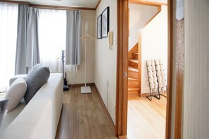 A modern living room with a sofa, a standing lamp, a coat rack, and a staircase leading to an upper floor.