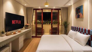 Une chambre d’hôtel moderne dotée d’un grand lit, d’un bureau avec un téléviseur à écran plat, d’un balcon agrémenté de plantes et d’un tableau au mur.