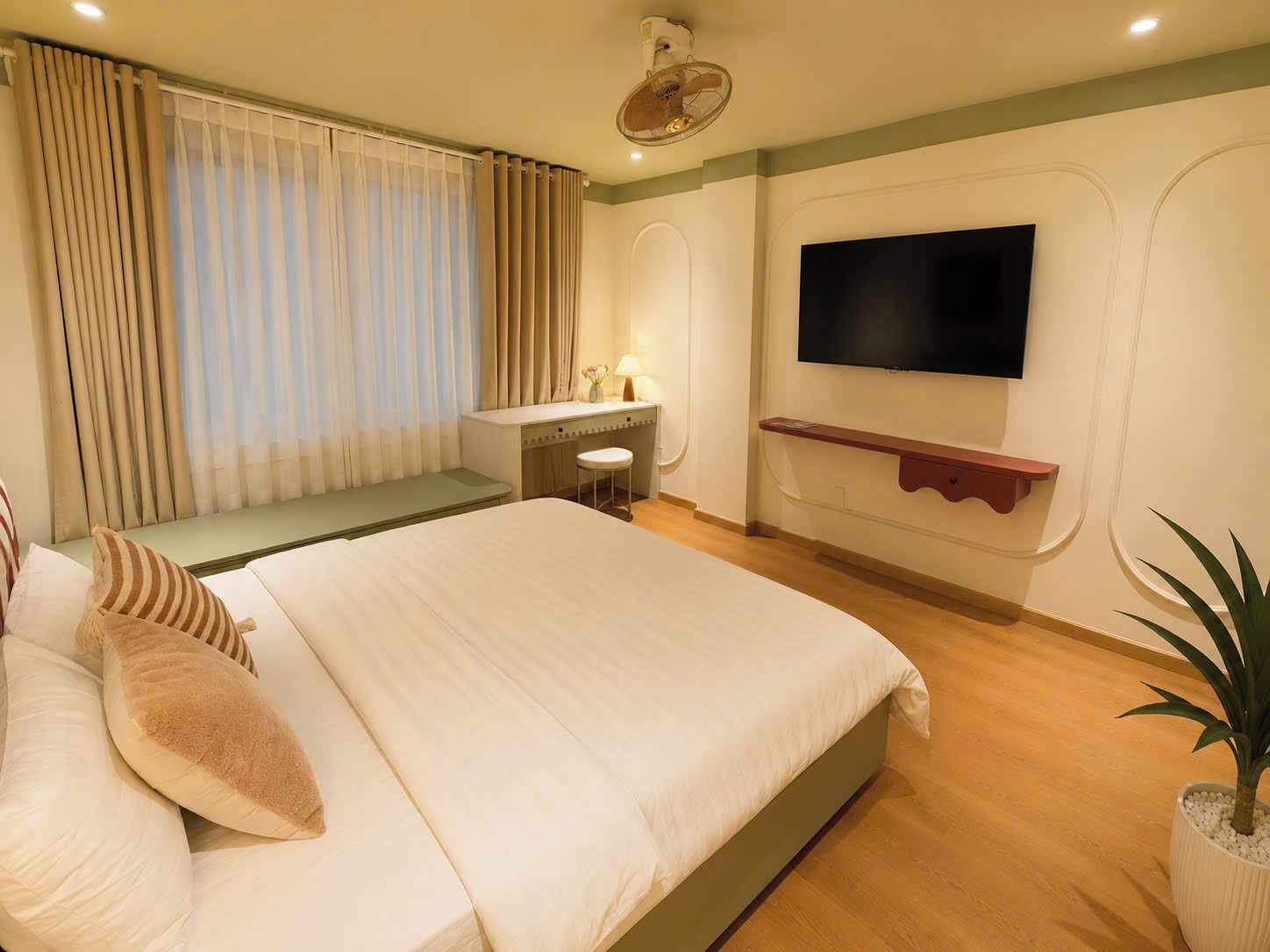 Een hotelkamer met een bed, een bureau, een stoel, een aan de muur bevestigde televisie en een potplant.