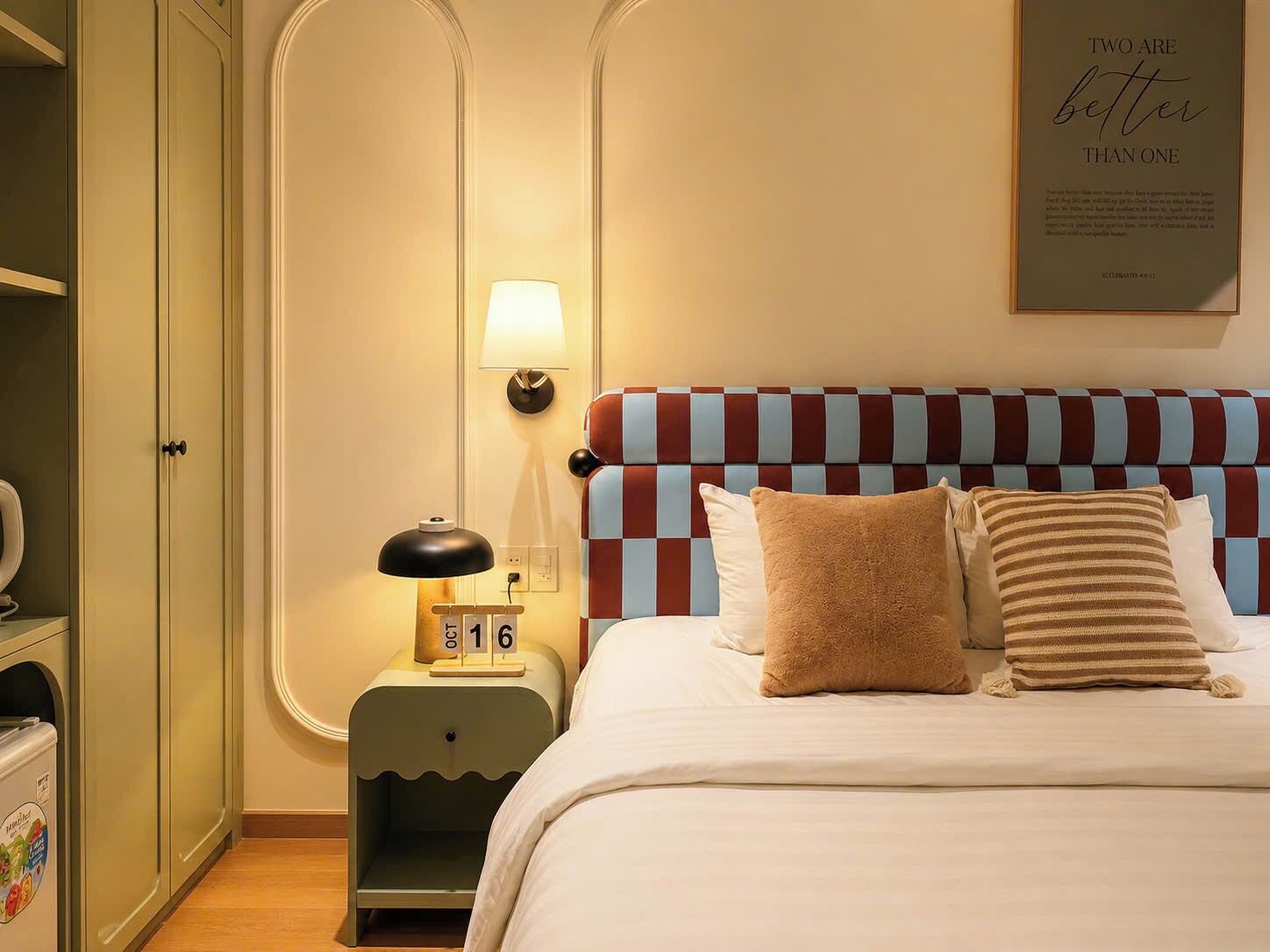 A neatly arranged bedroom with a checkered headboard, a bedside lamp, and a wall clock.