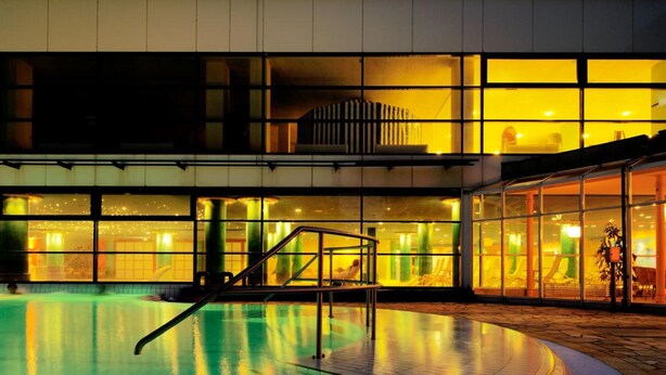 A swimming pool with a tiled deck, a covered area with glass walls, and a building with a flat roof. - Baltic Zinnowitz (Zinnowitz)