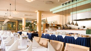 A restaurant with tables set for dining, a kitchen area, and hanging pendant lights. - Baltic Zinnowitz (Zinnowitz)