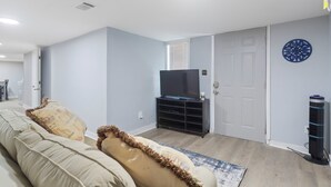 Ein Wohnzimmer mit Sofa, Fernseher auf einem Schrank, einer Tür und einem dekorativen Teller an der Wand.