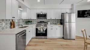 A modern kitchen with white cabinets, stainless steel appliances, a microwave, oven, and refrigerator. - Condo 12 Coastal Comfort (New Smyrna)