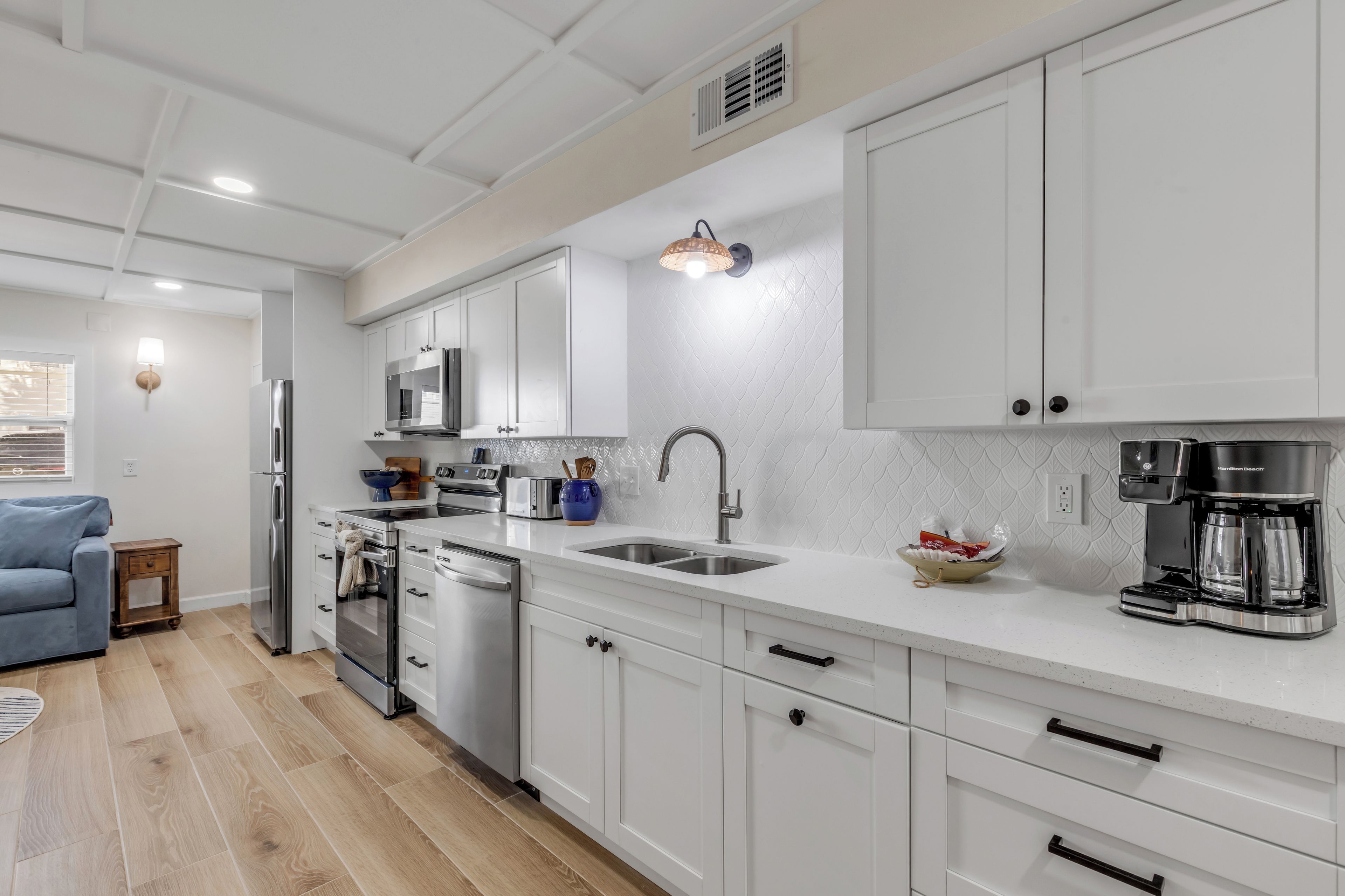 Una cocina moderna con muebles blancos, electrodomésticos de acero inoxidable y una cafetera.