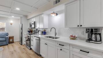 Una cocina moderna con muebles blancos, electrodomésticos de acero inoxidable y una cafetera.