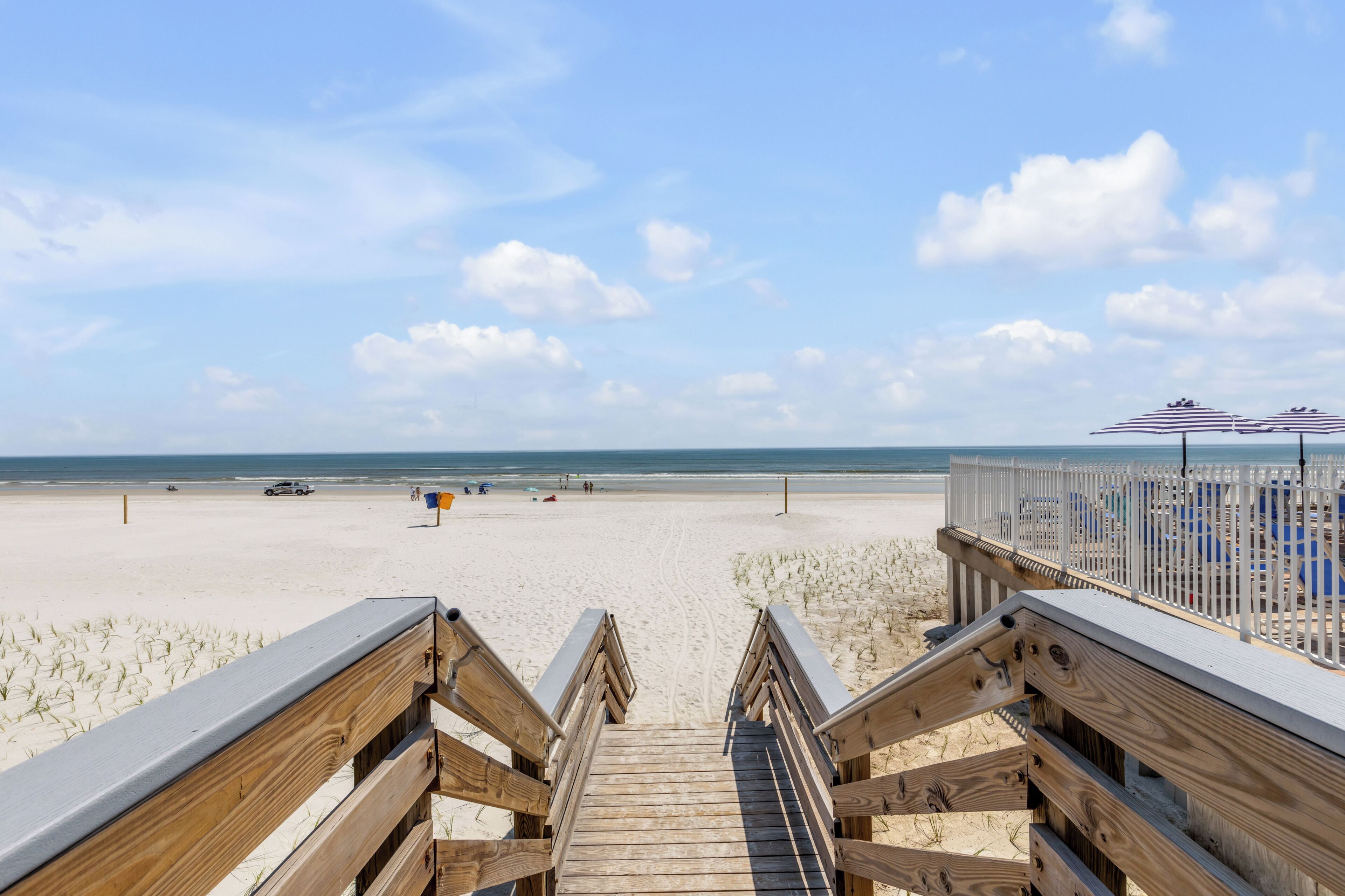 A wooden boardwalk leading to a beach with umbrellas and beach chairs.