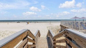 A wooden boardwalk leading to a beach with umbrellas and beach chairs. - Condo 12 Coastal Comfort (New Smyrna)