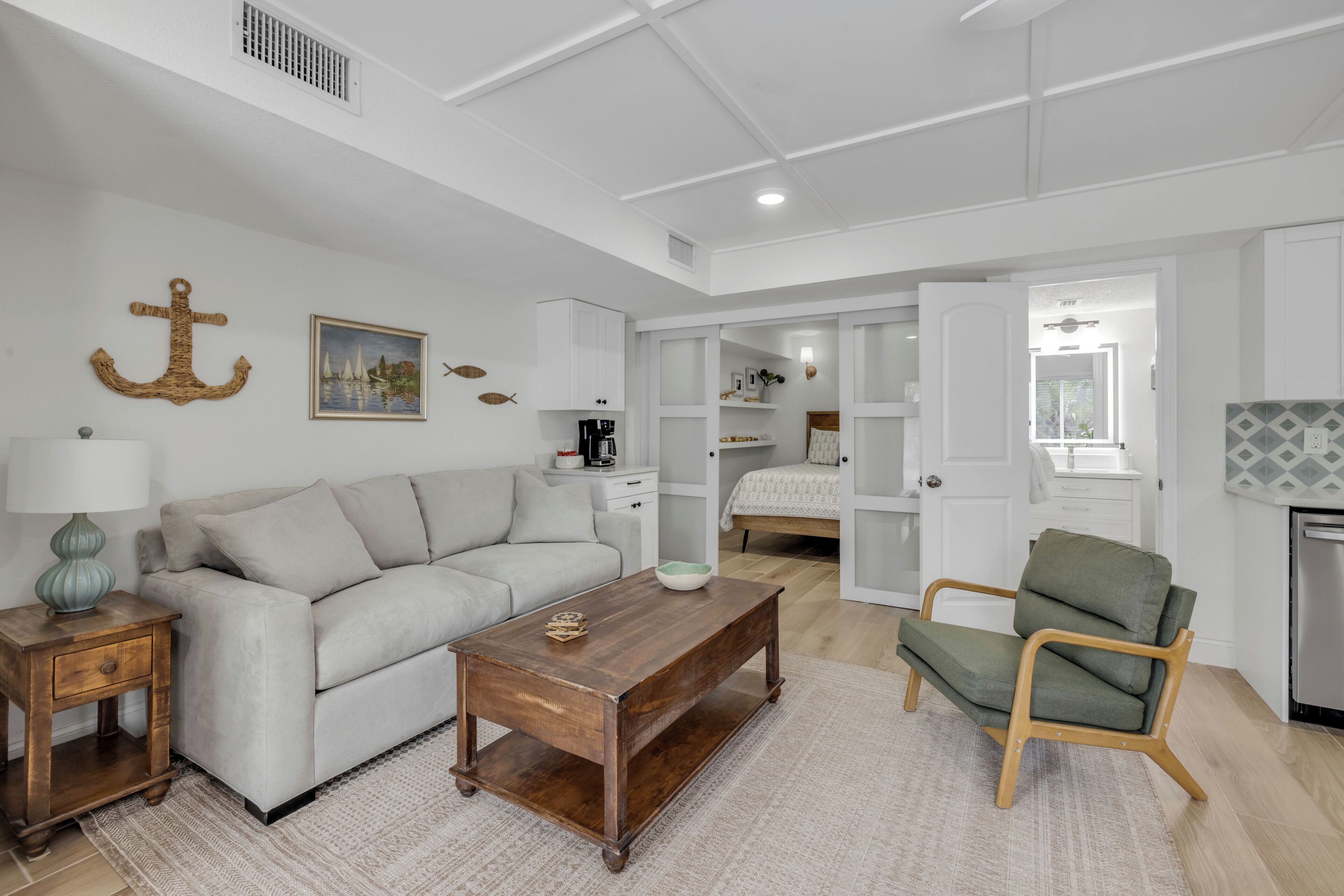 A modern living room with a sofa, coffee table, and armchair, a kitchen area with cabinets, and a dining table.