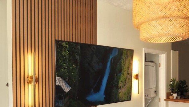 A modern interior with a mounted TV, wooden panel wall, and a hanging light fixture. - LUXURY DOWNTOWN COLUMBUS TOWNHOME (Columbus)