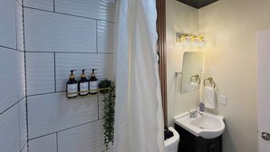 A bathroom with a white tiled wall, a shower curtain, a sink with a mirror, and toiletries on a shelf. - LUXURY DOWNTOWN COLUMBUS TOWNHOME (Columbus)