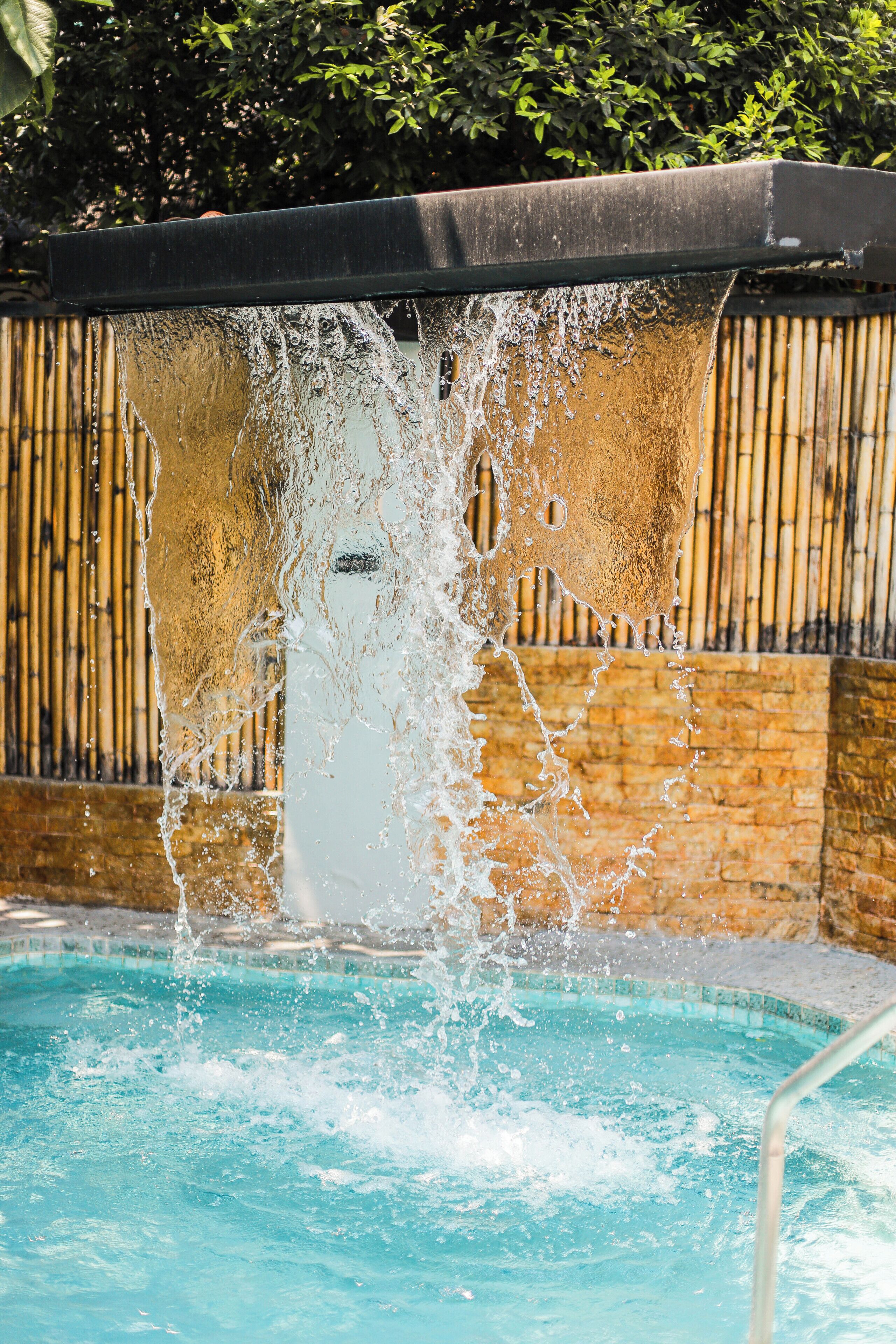 Una piscina con agua que cae por una pared, rodeada por una valla de bambú.