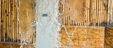 Una piscina con agua que cae por una pared, rodeada por una valla de bambú.