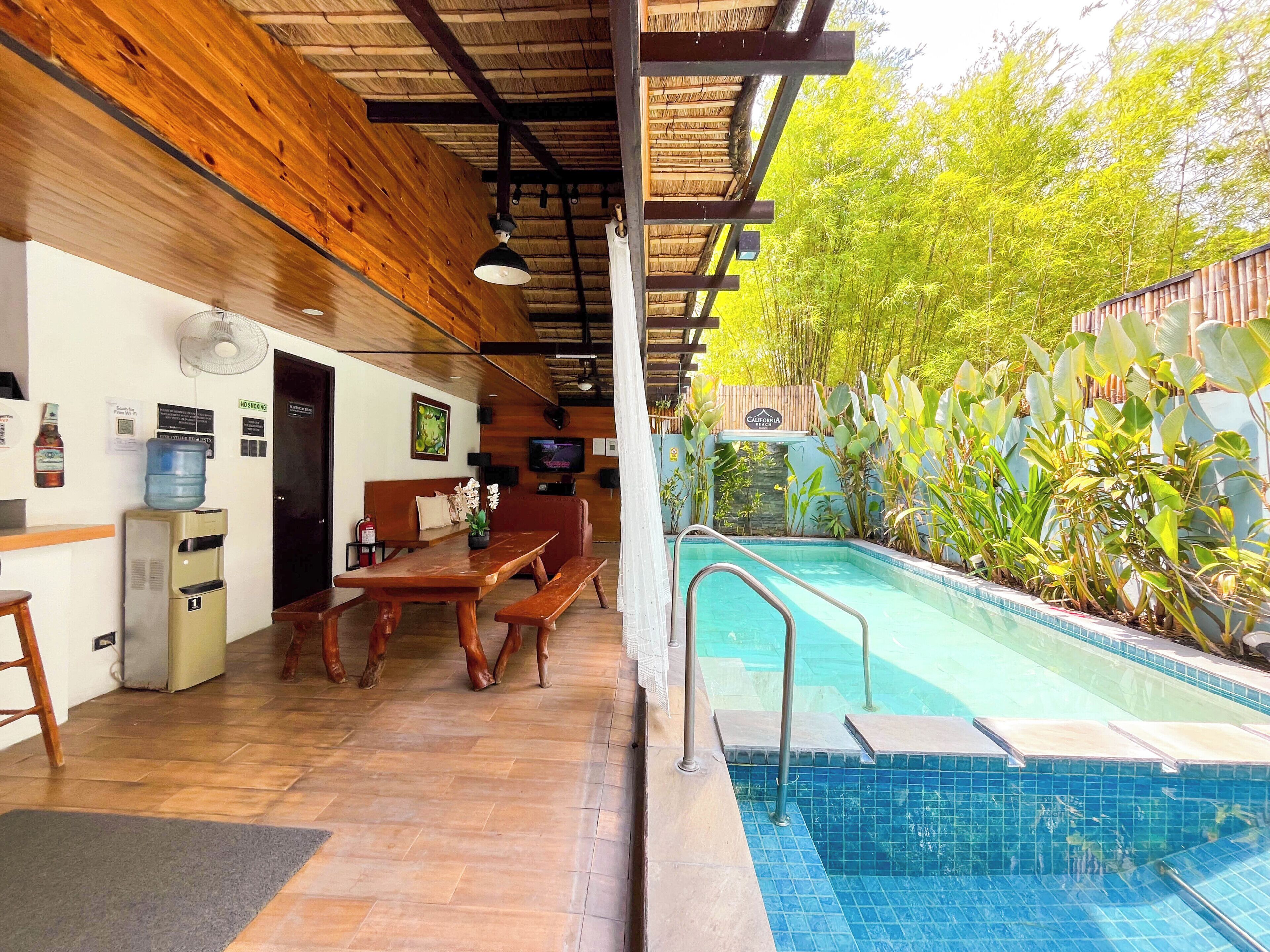 A pool area with a wooden deck, a table, chairs, a water dispenser, and a television.