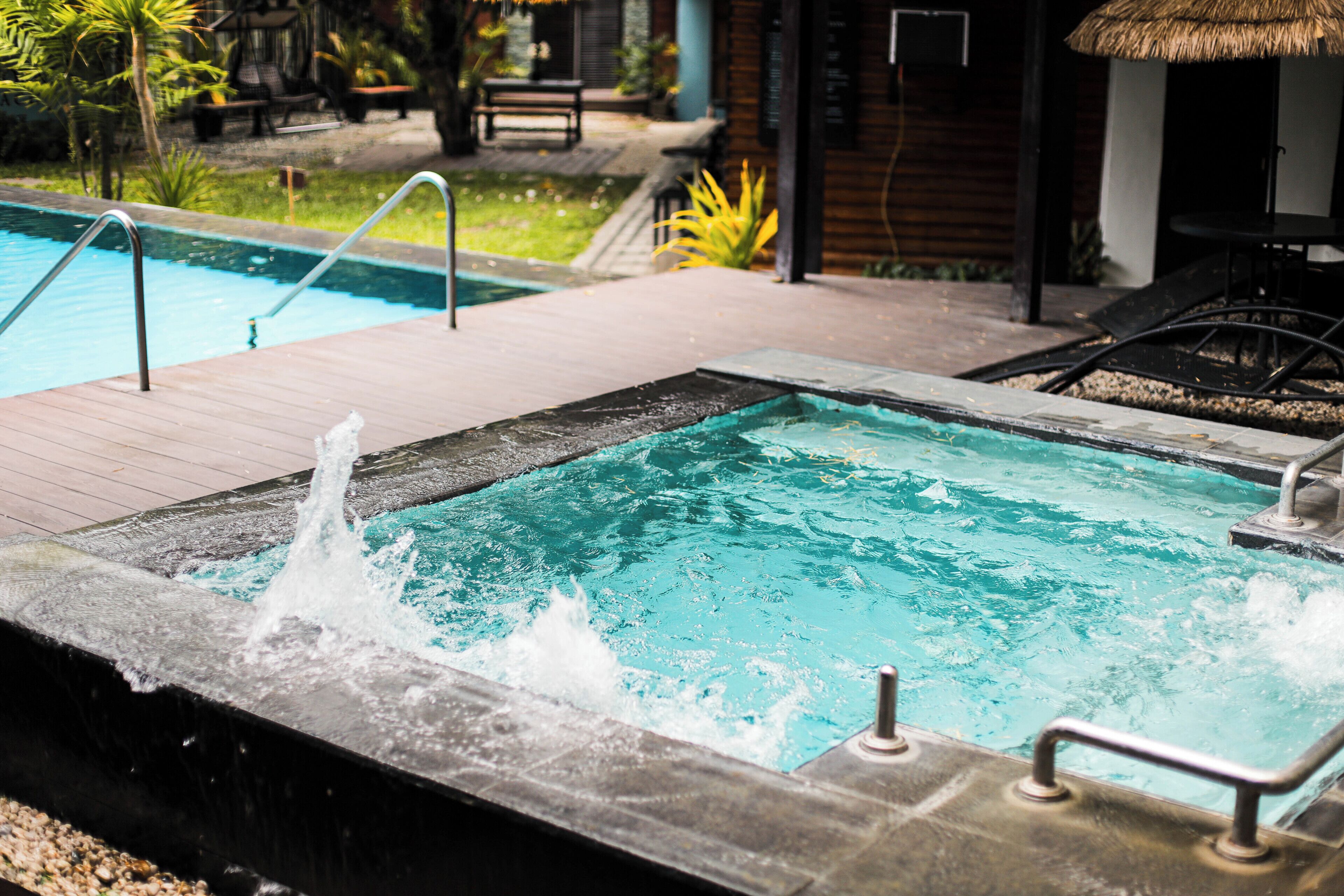 Una piscina con hidromasaje, rodeada por una terraza de madera y mobiliario de exterior.
