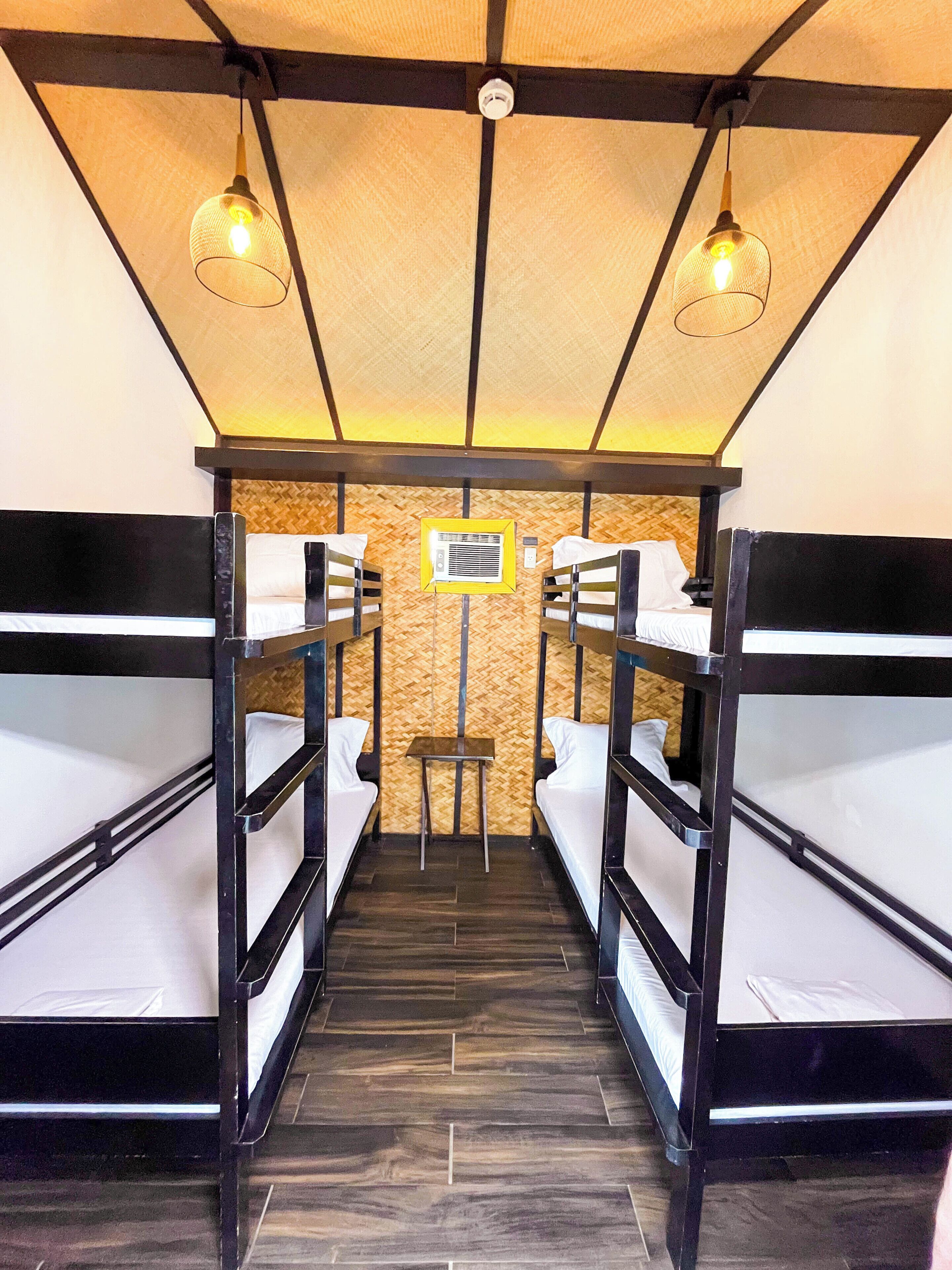 A bunk room with four beds, a small table, and two hanging lights.