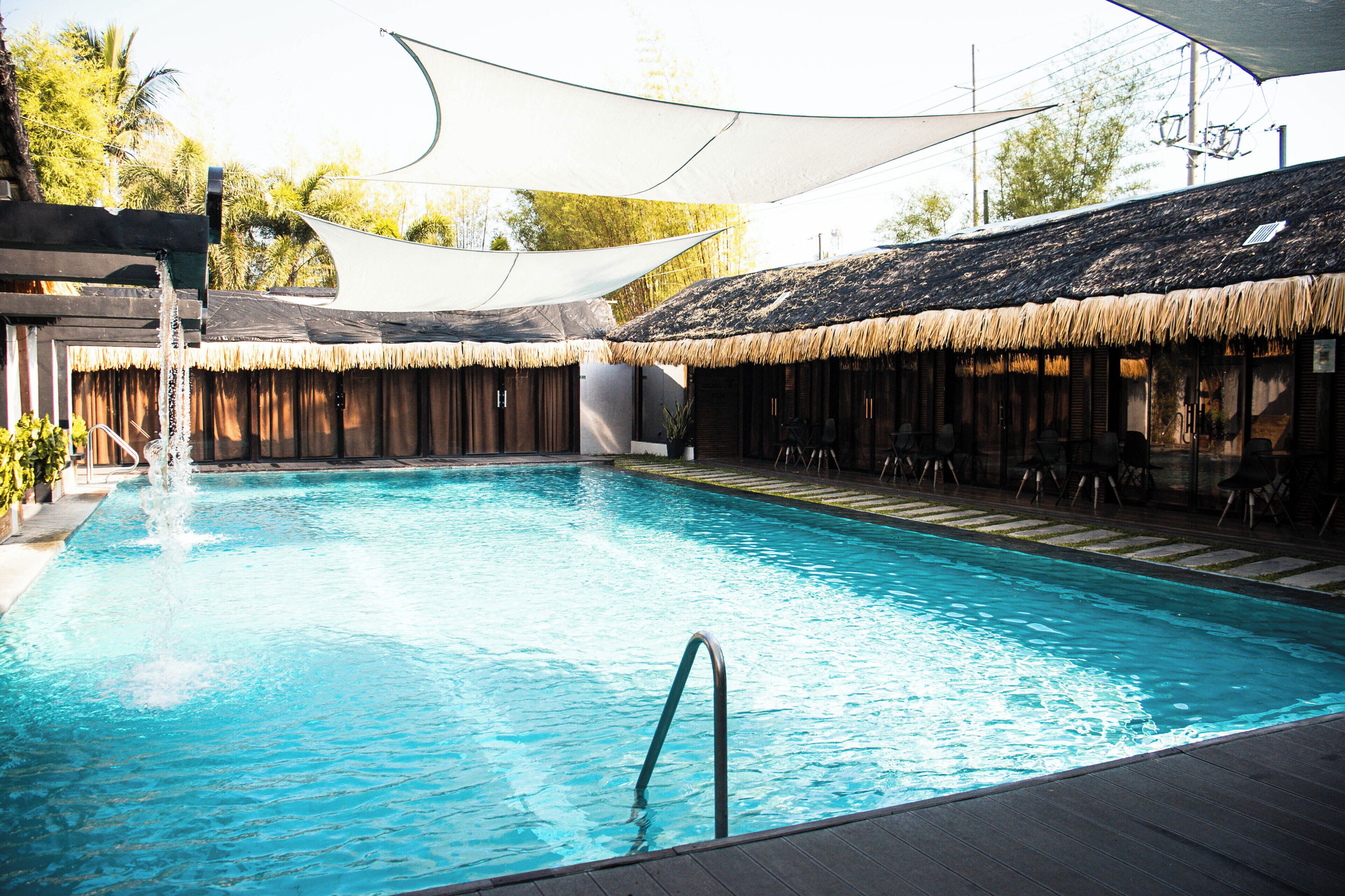 A swimming pool with a thatched roof area and a wooden deck.