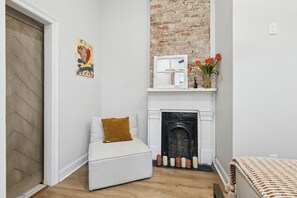 A room with a fireplace, a small seating area with a cushion, a wall-mounted shelf with flowers, and a door with a herringbone pattern. - Uptown Oasis - 1 Mile from Caesar Superdome (New Orleans)
