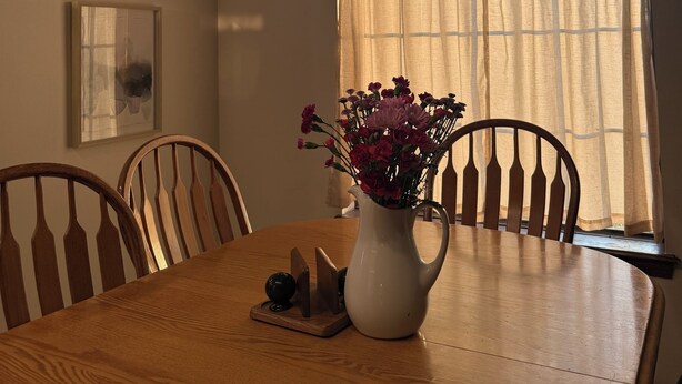 Ett matbord med stolar, en vas med blommor och ett fönster med gardiner.