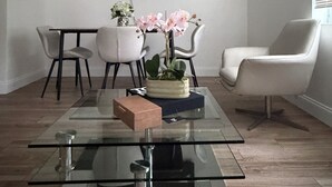 Ein modernes Wohnzimmer mit einem Glastisch, einem flachbildfernseher an der Wand und einem Blumentopf mit rosa Blüten.