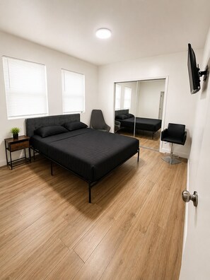 A bedroom with a bed, a chair, a bedside table, a mirror, and a TV mounted on the wall. - Lovely 3-bedroom house with AC in soothing Hollywood (Hollywood)