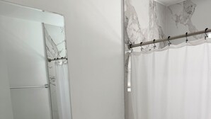 Ein Badezimmer mit Wand in Marmoroptik, einem weißen Waschbecken mit Seifenspender, einer Toilette und einer Duschvorhang.