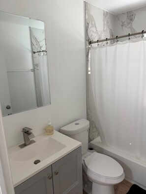 Ein Badezimmer mit Wand in Marmoroptik, einem weißen Waschbecken mit Seifenspender, einer Toilette und einer Duschvorhang.