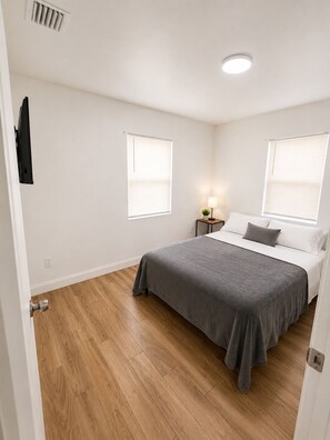 A bedroom with a bed, two windows, a nightstand with a lamp, and a door. - Lovely 3-bedroom house with AC in soothing Hollywood (Hollywood)