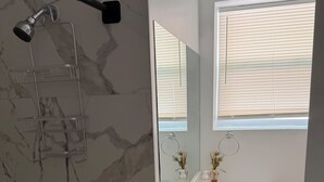 Ein Badezimmer mit Dusche, Waschbecken, Spiegel und Fenster.