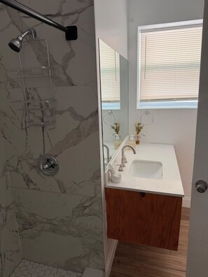 Ein Badezimmer mit Dusche, Waschbecken, Spiegel und Fenster.