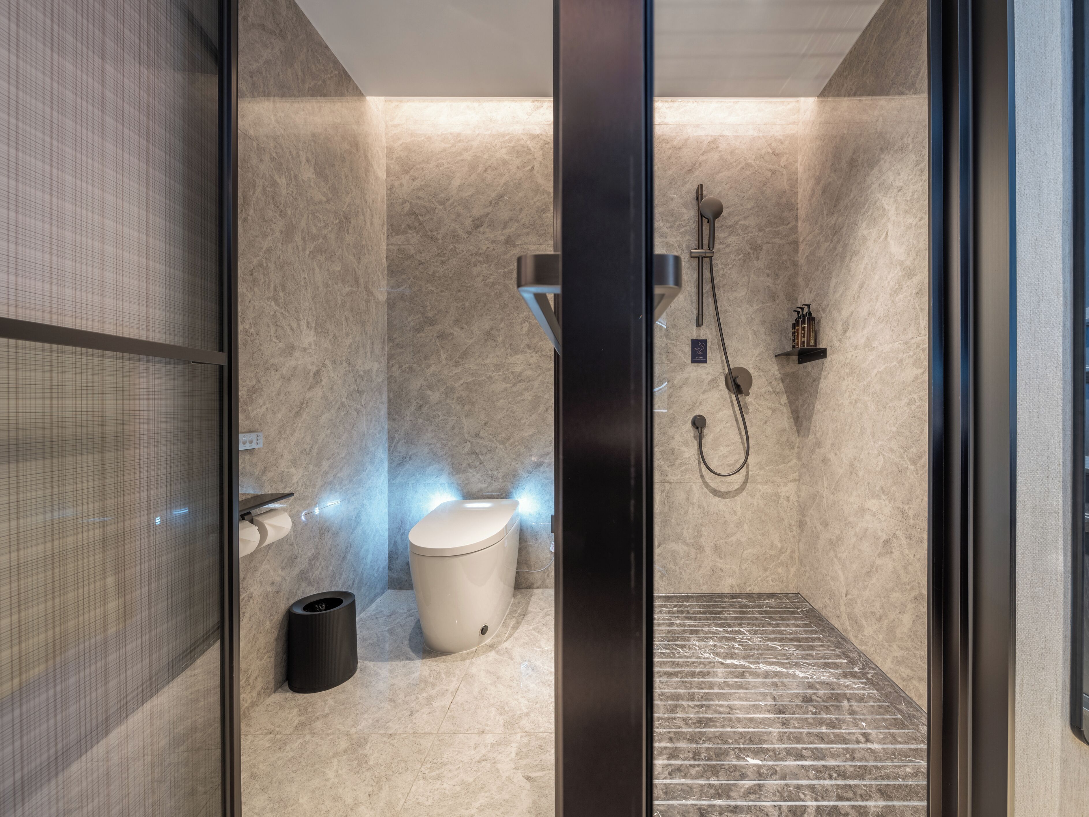 Une salle de bain moderne avec une paroi en verre, des toilettes, une douche et une poubelle noire.