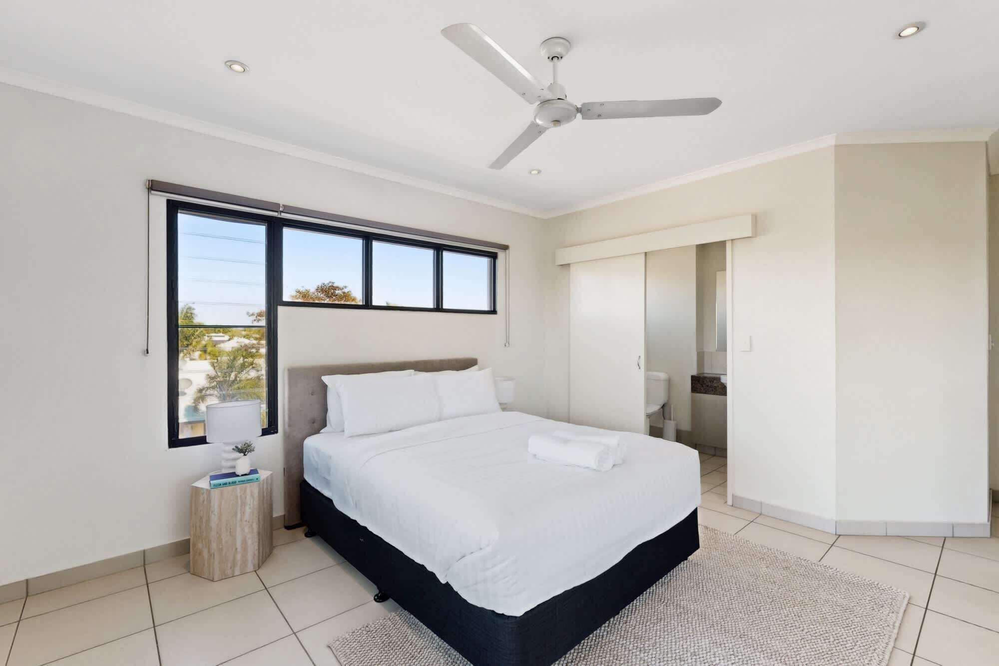 A modern bedroom with a bed, a ceiling fan, a window, and a view of the outdoors.