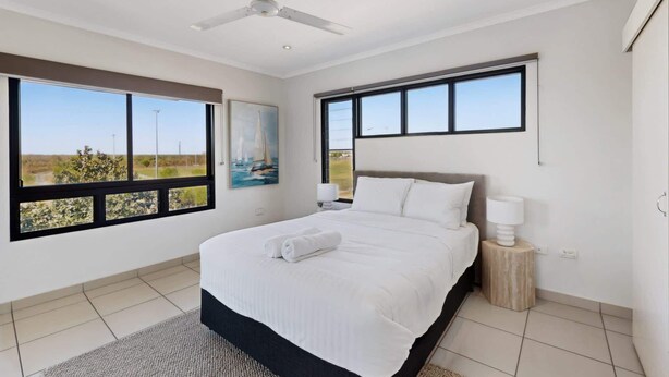 A bedroom with a bed, a ceiling fan, a nightstand, a lamp, and large windows with a view. - Peaceful 2-Bed Apartment with Private BBQ Balcony (Rosebery)