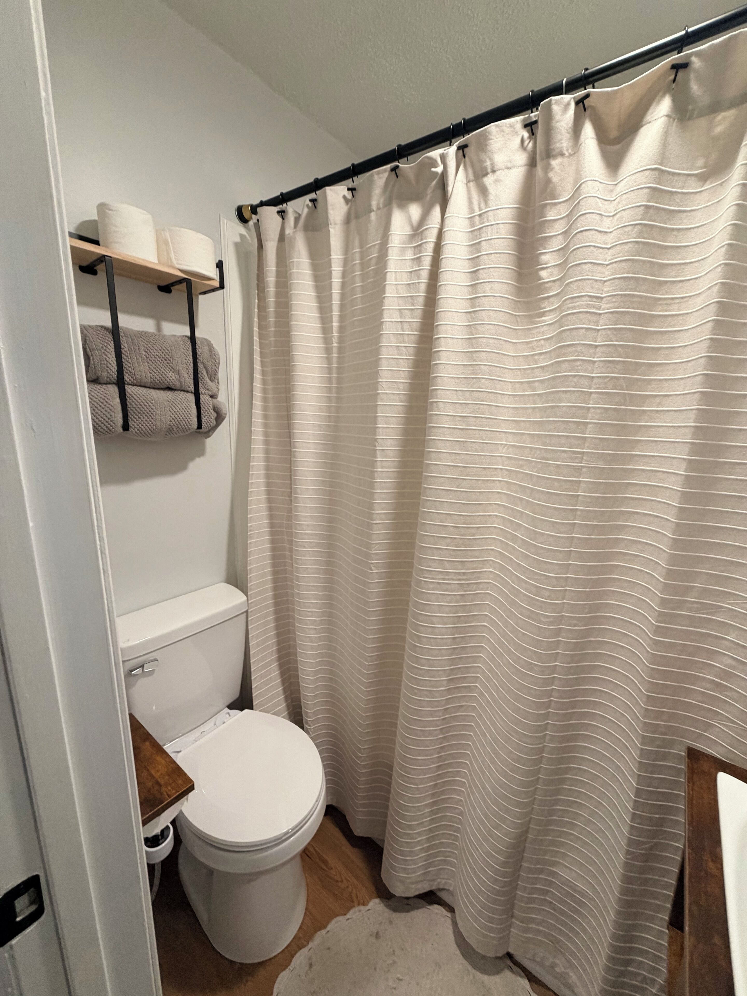 Ett badrum med en toalett, en duschdraperi och en handduksställning med handdukar.