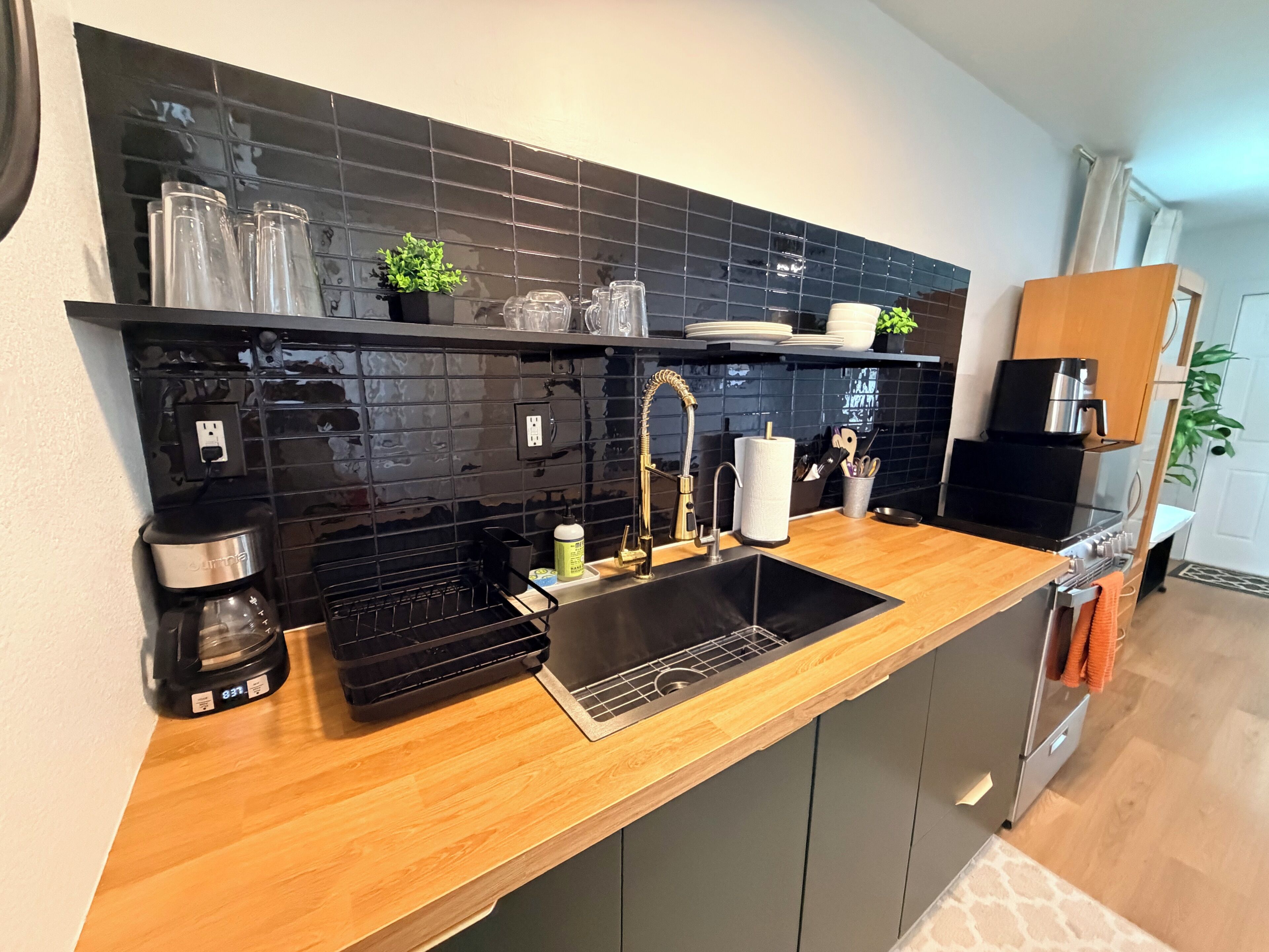 A modern kitchen with a black tiled backsplash, stainless steel appliances, and a wooden countertop.