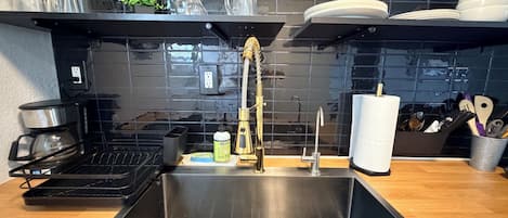 Una cocina moderna con un lavamanos de acero inoxidable, una cafetera y una alacena para vinos.