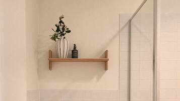 A bathroom with a toilet, a shelf with a plant, and a glass shower enclosure.