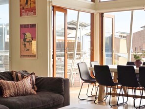 A modern living room with a sofa, a dining table with chairs, and a large sliding glass door leading to an outdoor area.