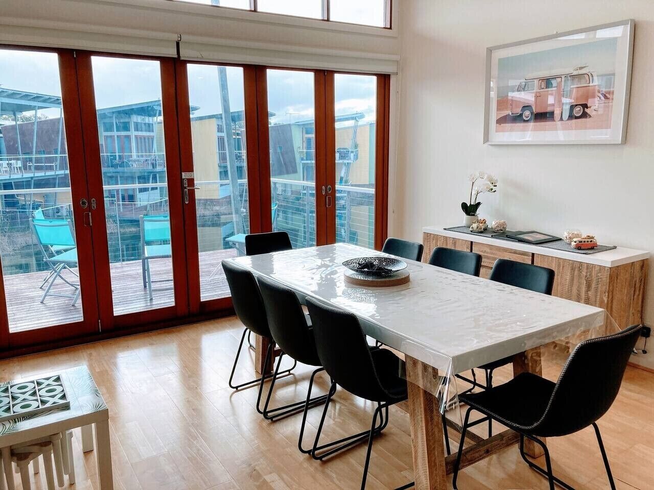 A modern dining area with a large table, black chairs, and a view through large glass doors.