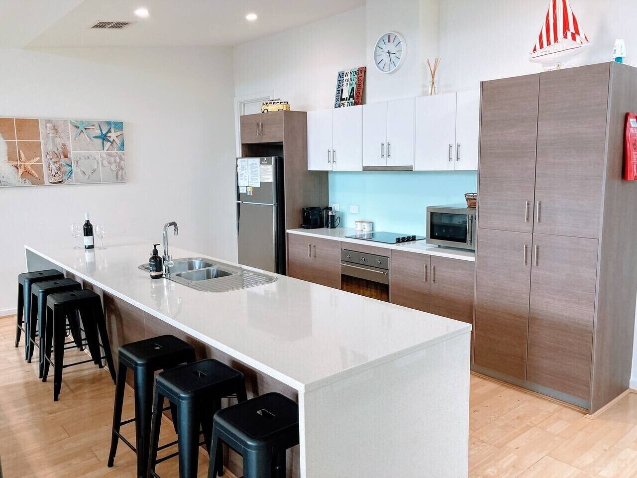 A modern kitchen with a central island, bar stools, a refrigerator, microwave, and cabinets.