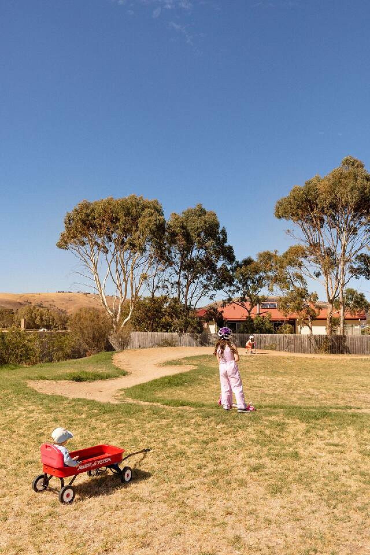 A child playing in a grassy backyard with trees and a house in the background.