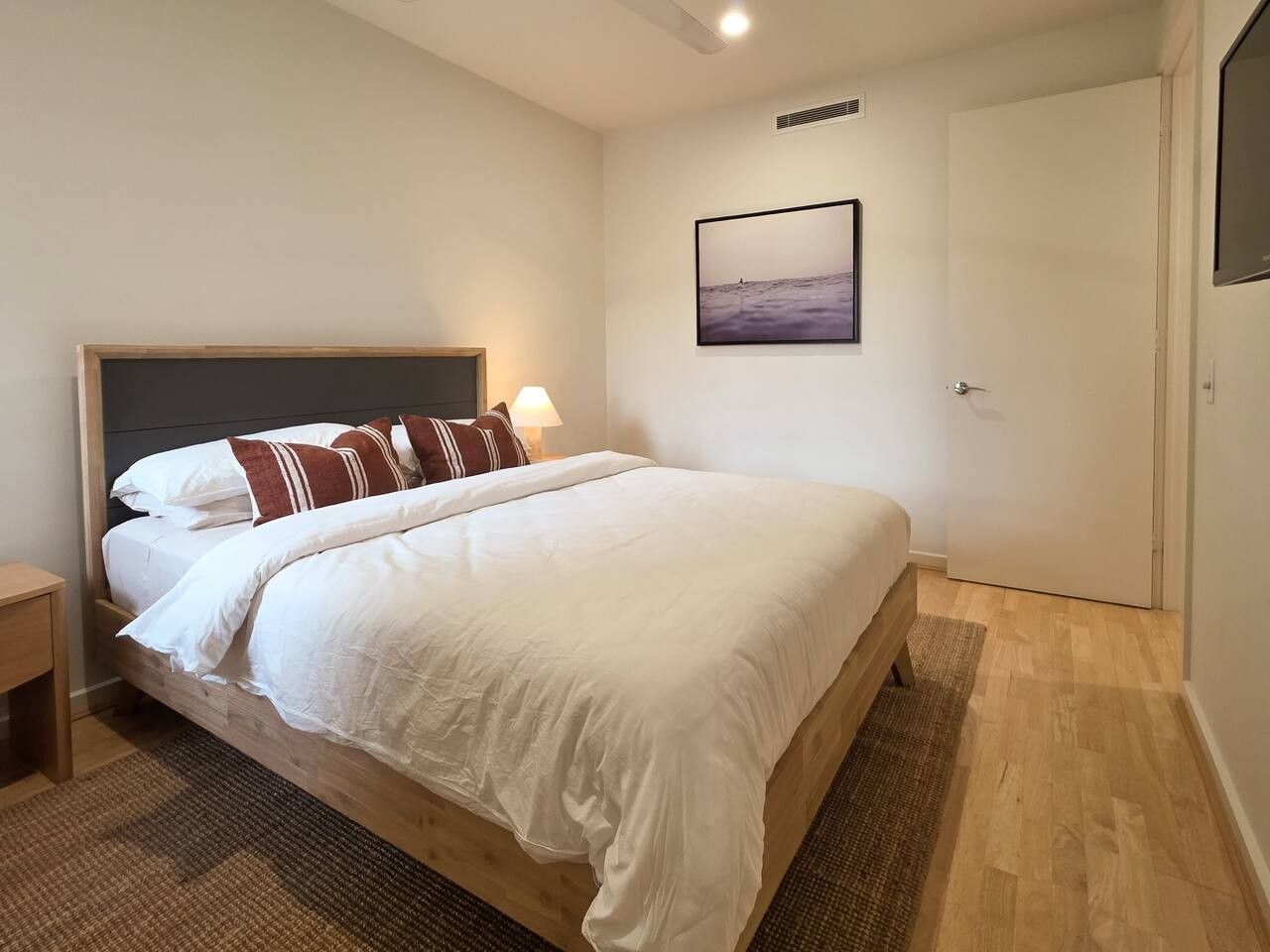 A bedroom with a bed, a nightstand, a wall-mounted picture, and a door.