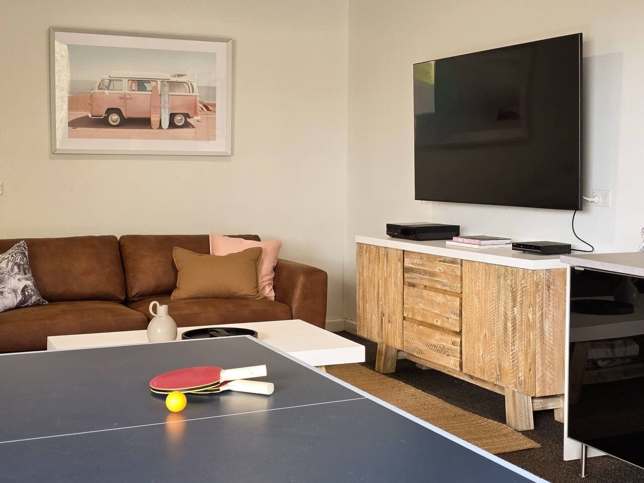Un salon avec une table de ping-pong, un canapé, un téléviseur et un meuble en bois.