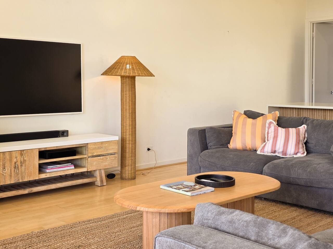 Un salon moderne avec un téléviseur à écran plat, une table basse ronde en bois, un canapé gris avec des coussins à rayures et un grand lampadaire.