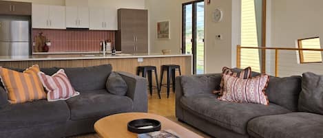 A modern living room with two grey sofas, a wooden coffee table, and a kitchen in the background.