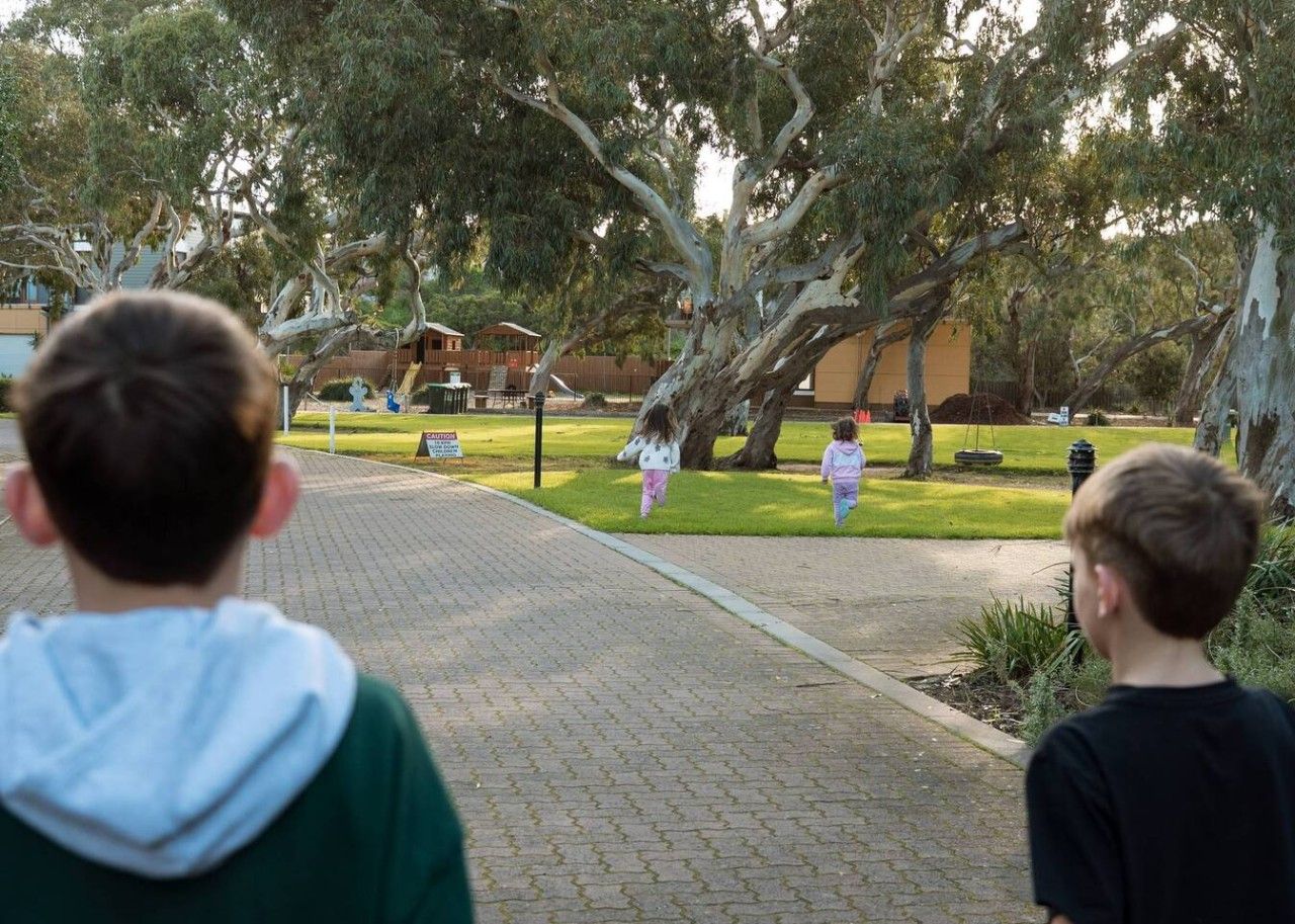 A paved pathway in a park with trees and a building in the background.