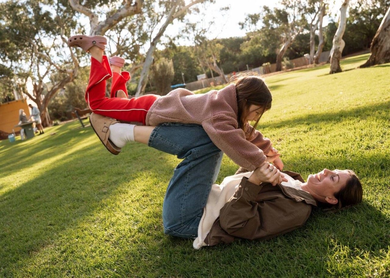 A person lying on grass with another person sitting on their back.