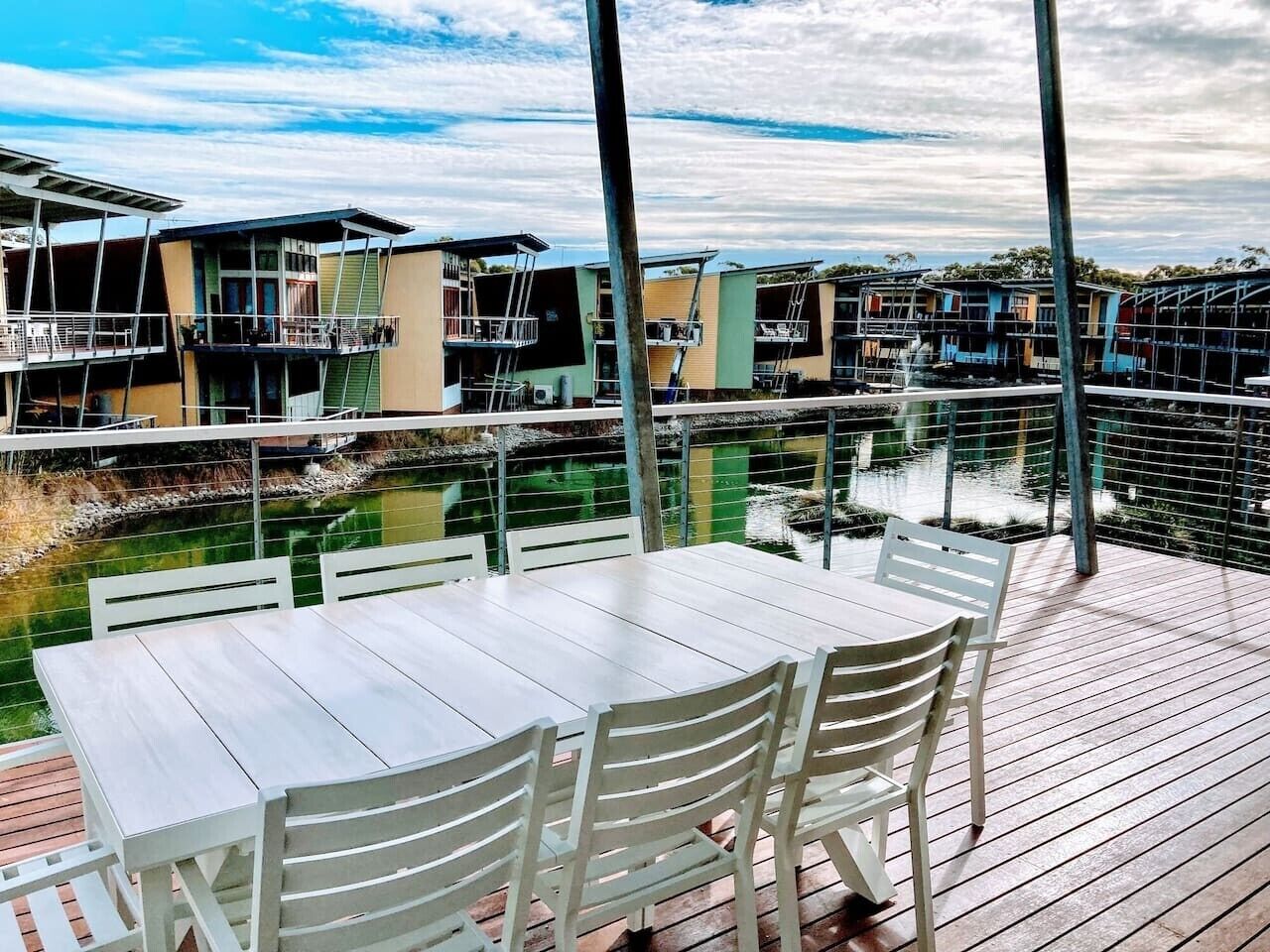 A deck with a table and chairs overlooking a water body with buildings in the background.