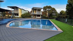 Una piscina con bordo in legno ed erba sintetica, circondata da edifici.