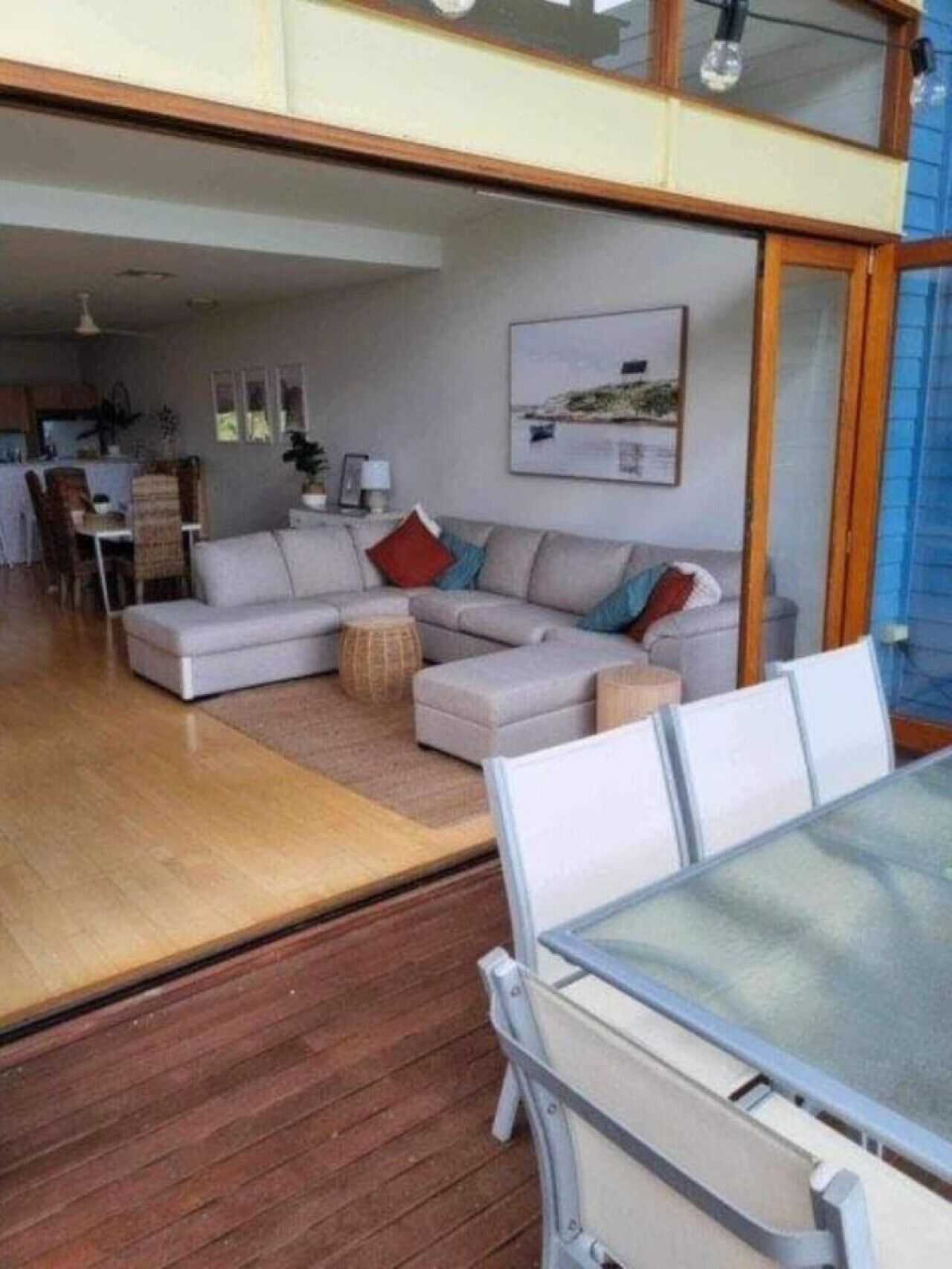 A spacious living area with a sofa set, a dining table, and a view through a glass door.
